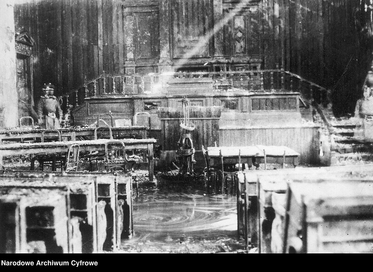 Interior of a gutted parliamentary chamber with blackened benches, collapsed fittings and a pool of water on the floor.