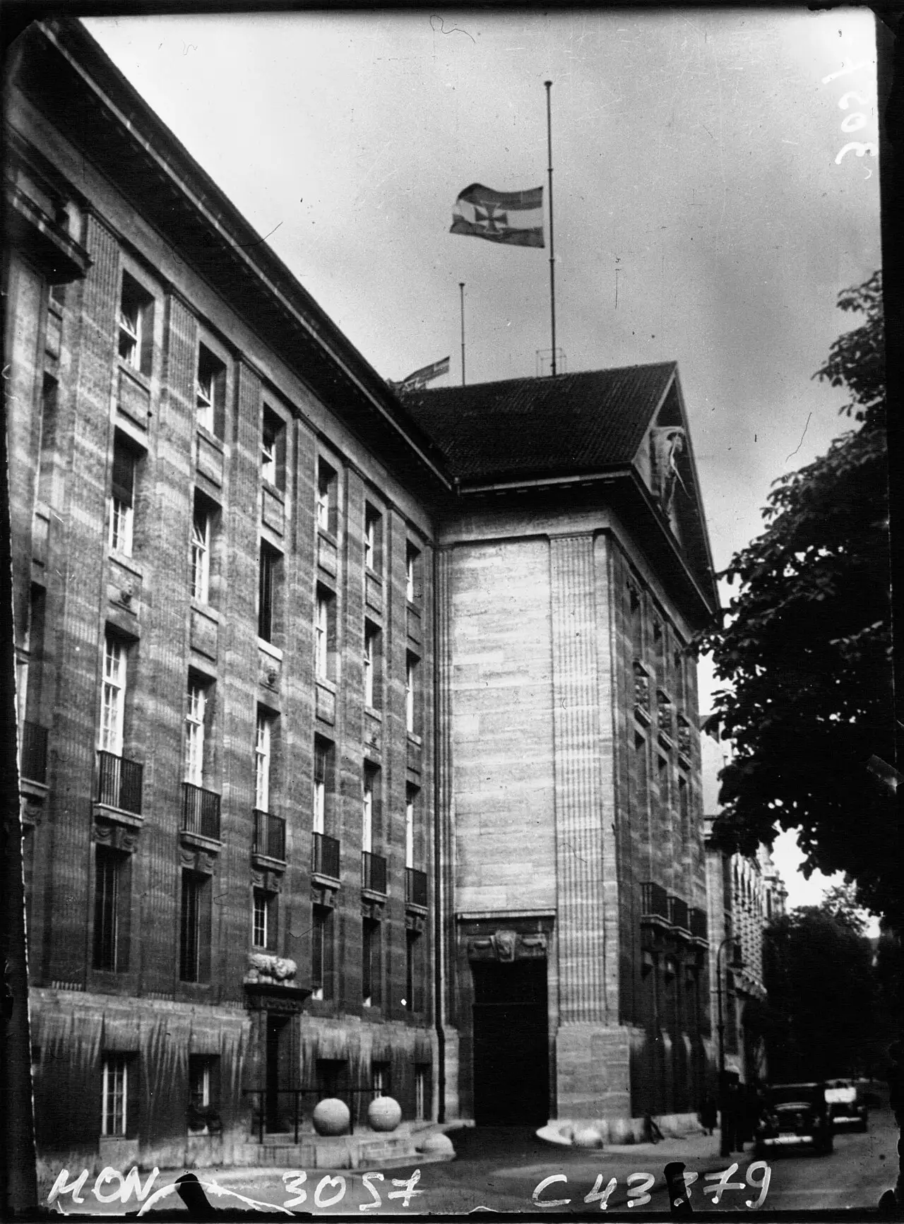 A large stone office building with a flag at half-mast on its roof