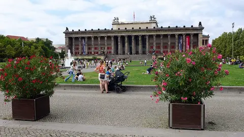 People on a lawn in front of a long colonnaded museum building, with flowering oleanders in planters in the foreground
