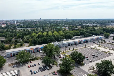 Aerial view of a long, low grandstand with a flat roof beside car parks, with woodland and the city beyond