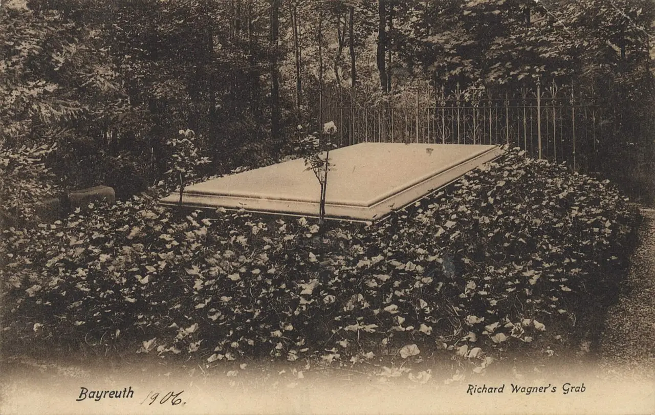 Postcard view of a large flat stone grave slab surrounded by ivy and trees in a garden.