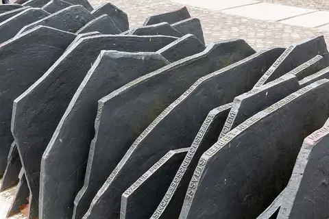 Rows of dark metal plates standing on edge in a paved square, with lettering along their upper edges
