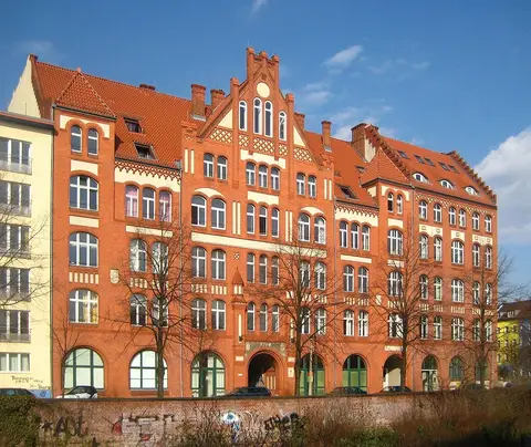 A long red-brick building with stepped gables and arched ground-floor windows behind bare trees