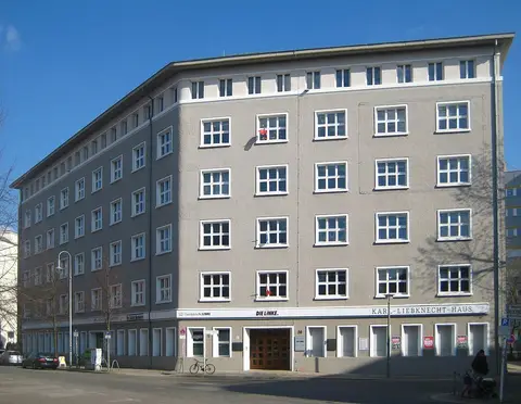 A five-storey grey corner building with rows of white-framed windows and the name Karl-Liebknecht-Haus above the ground floor