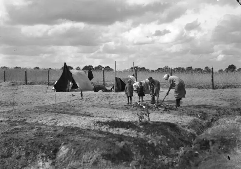 People digging and hoeing a field with small houses in the distance