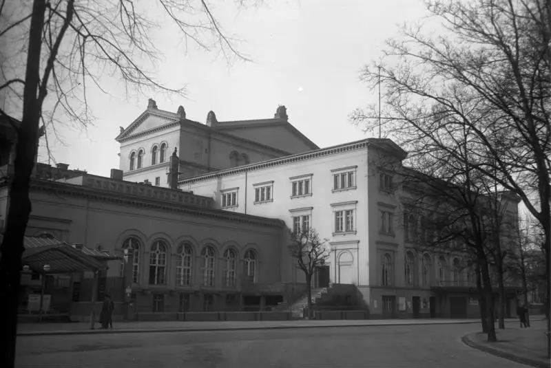 A large classical theatre building with a pedimented stage house and arched windows, seen across an empty street with bare trees.