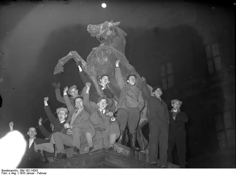 Young men in caps raise their fists on a large bronze horse statue at night