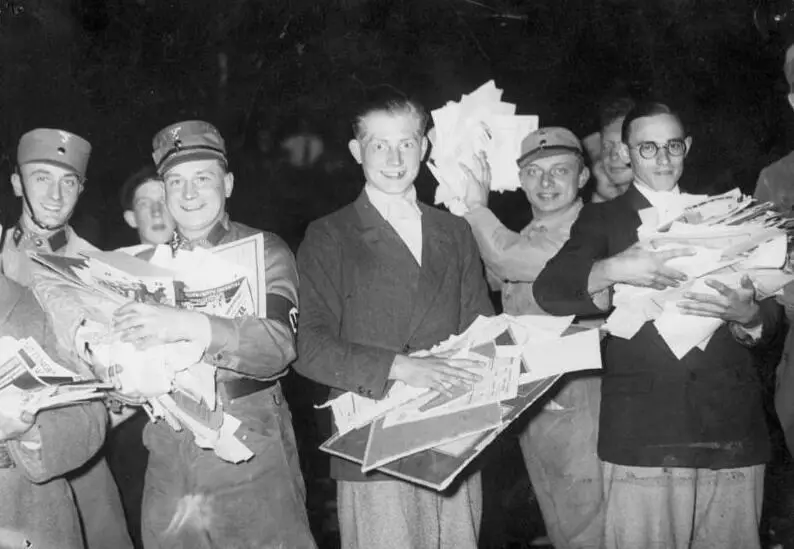 Grinning young men, several in SA caps and armbands, holding armfuls of papers and journals