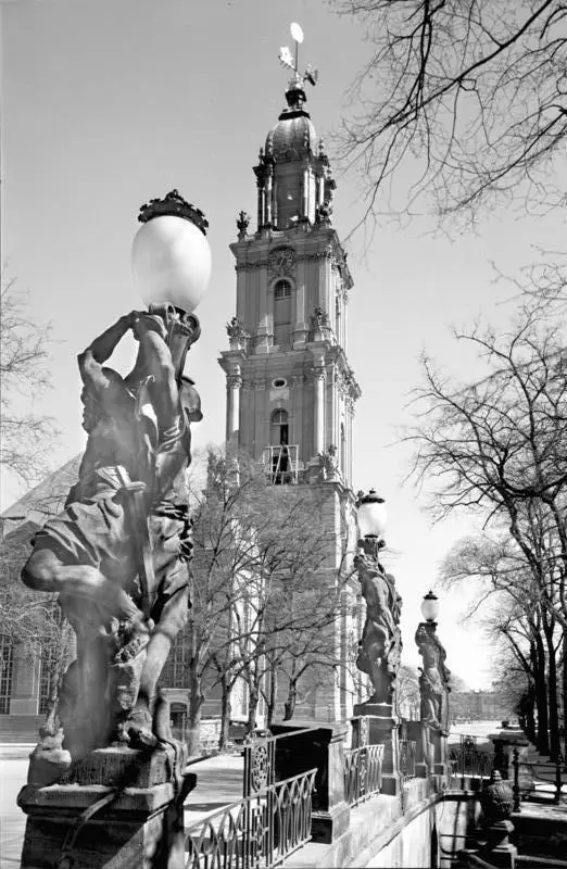 The tall baroque tower of the Garrison Church rising behind lamp-bearing statues on a canal bridge, with bare trees on either side.