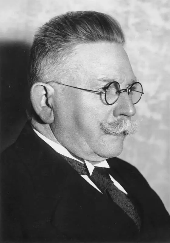 Portrait of a man with a white moustache and short white hair in a dark suit