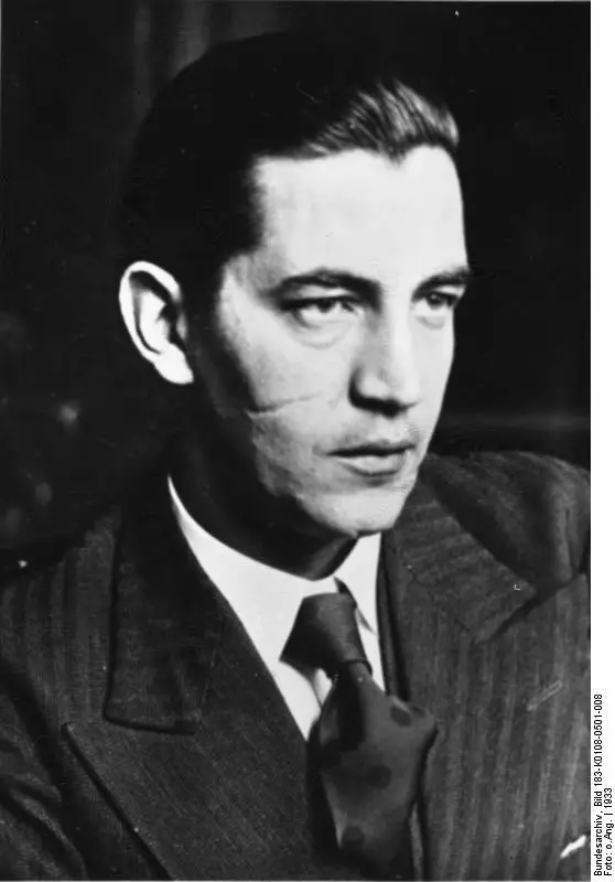Studio portrait of a man with dark slicked-back hair in a suit and tie