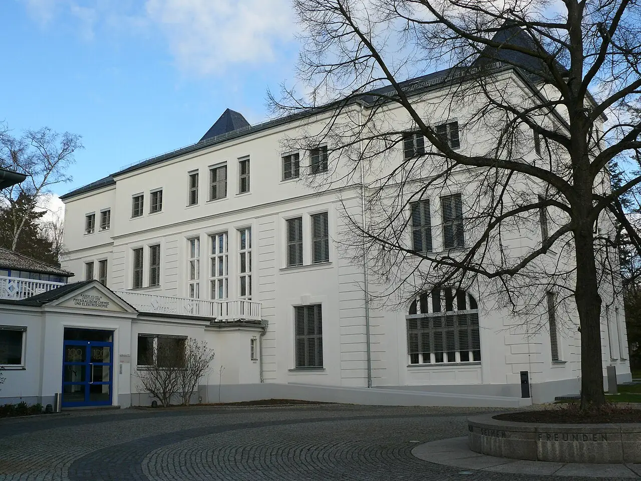 A brick institute building with a pitched roof behind trees in winter