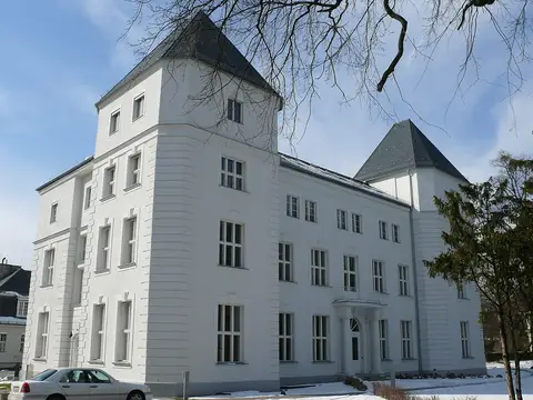 A white institute building with two pyramid-roofed corner towers, with snow on the ground