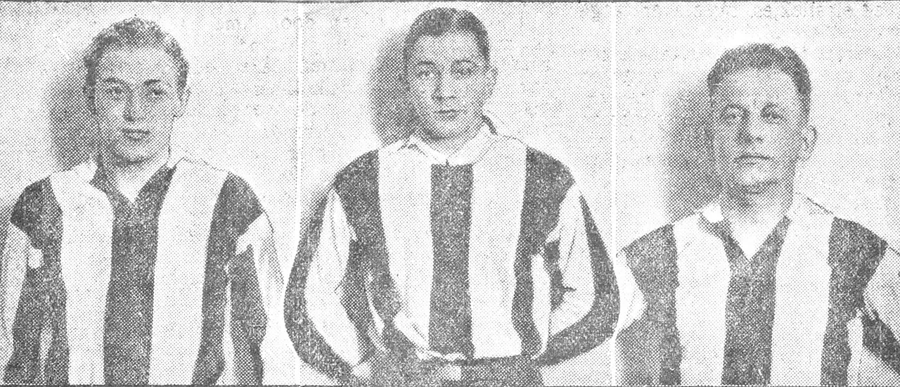 Three young men in ice hockey kit stand side by side holding sticks.