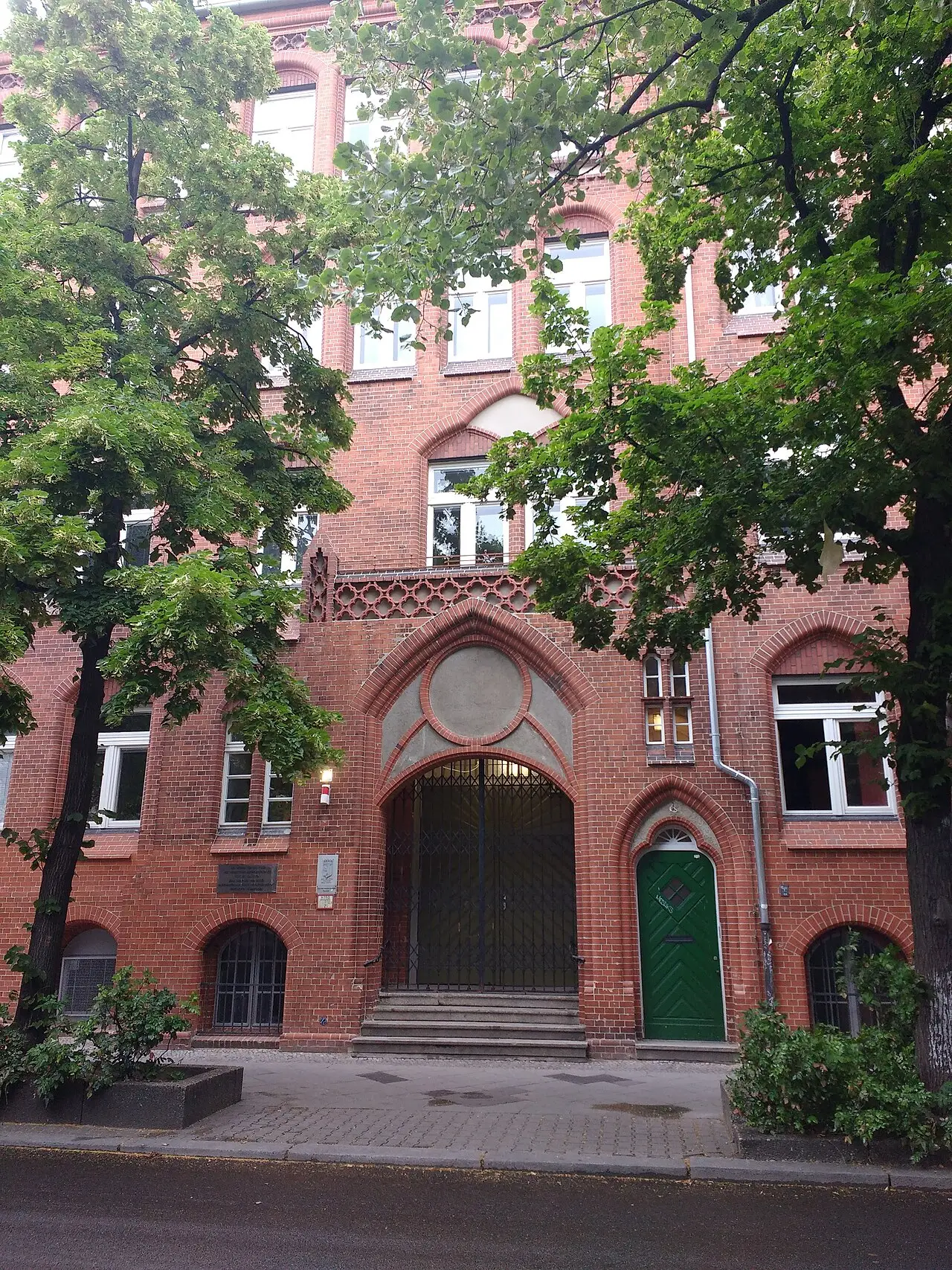 A brick school entrance with a heavy wooden door and a small bronze plaque on the wall beside it.