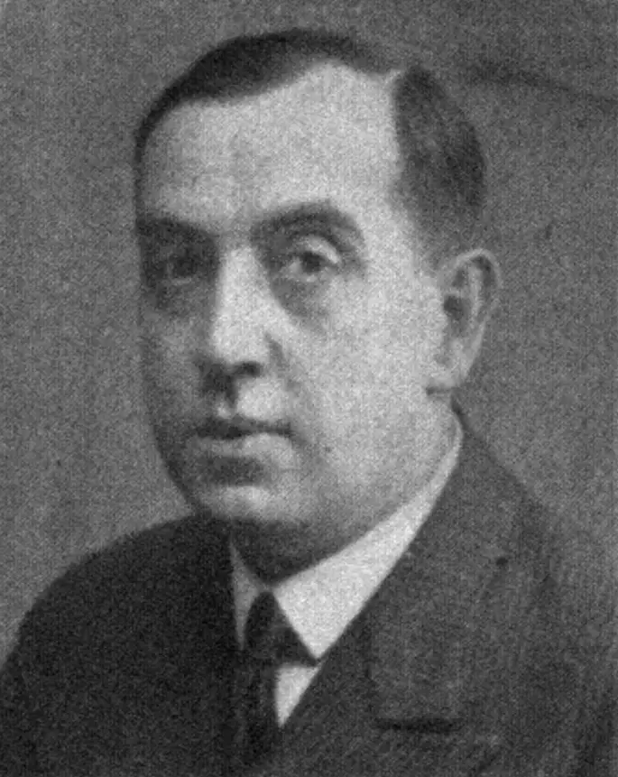Head-and-shoulders portrait of a man with receding dark hair, in a dark suit and tie.