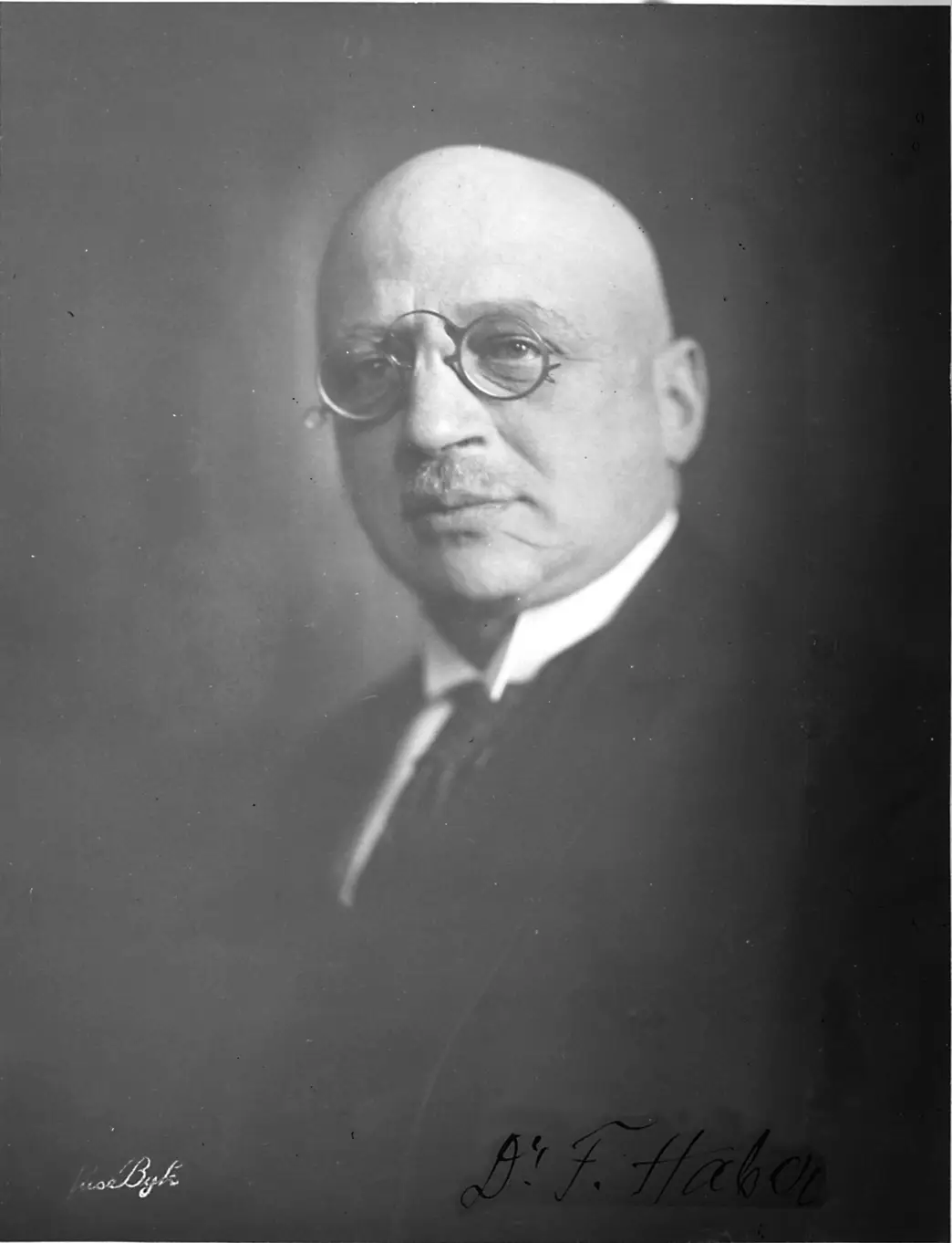 Portrait of a bald man with a moustache and round glasses in a dark suit