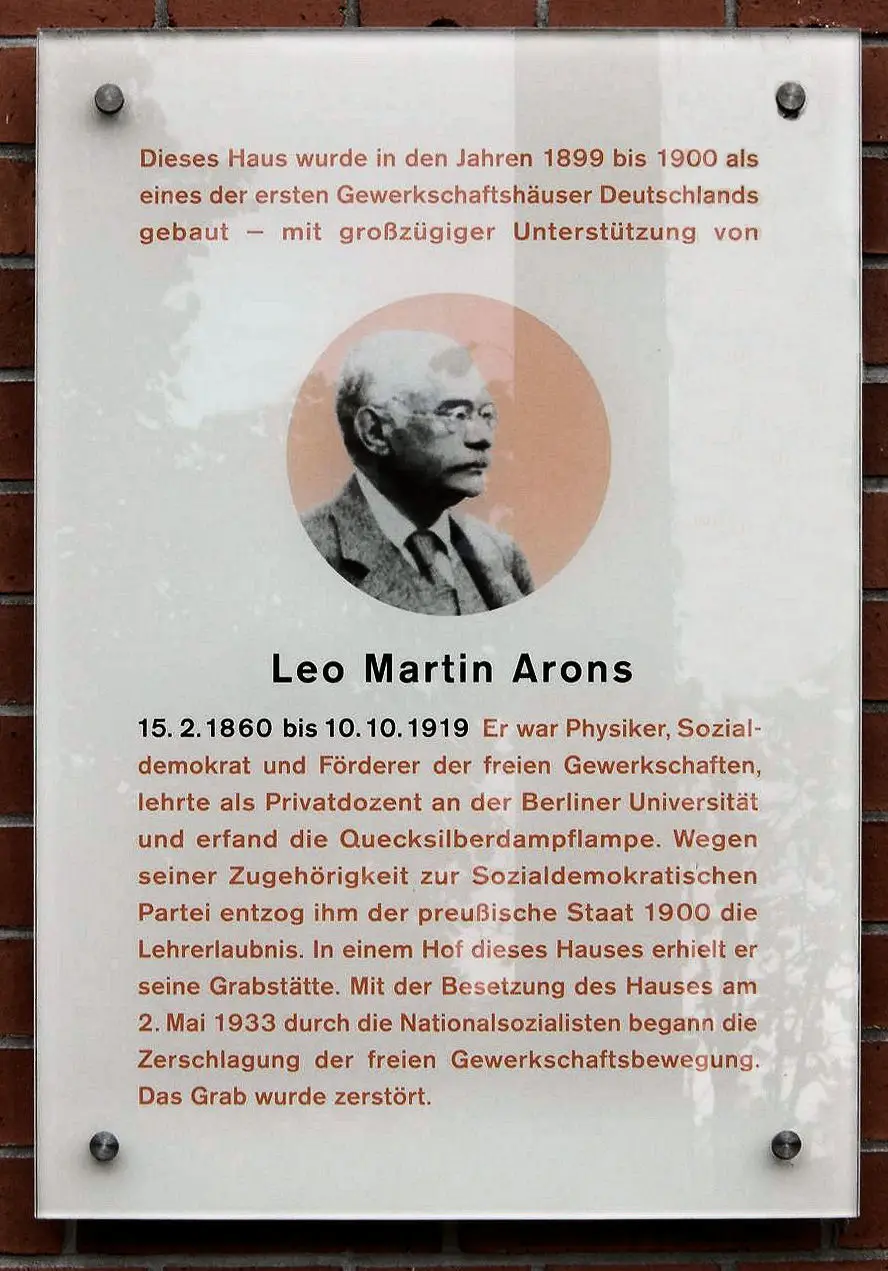 A glass plaque with text and a small portrait mounted on a building wall