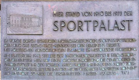 A bronze plaque with a relief of the Sportpalast facade beside a block of engraved German text