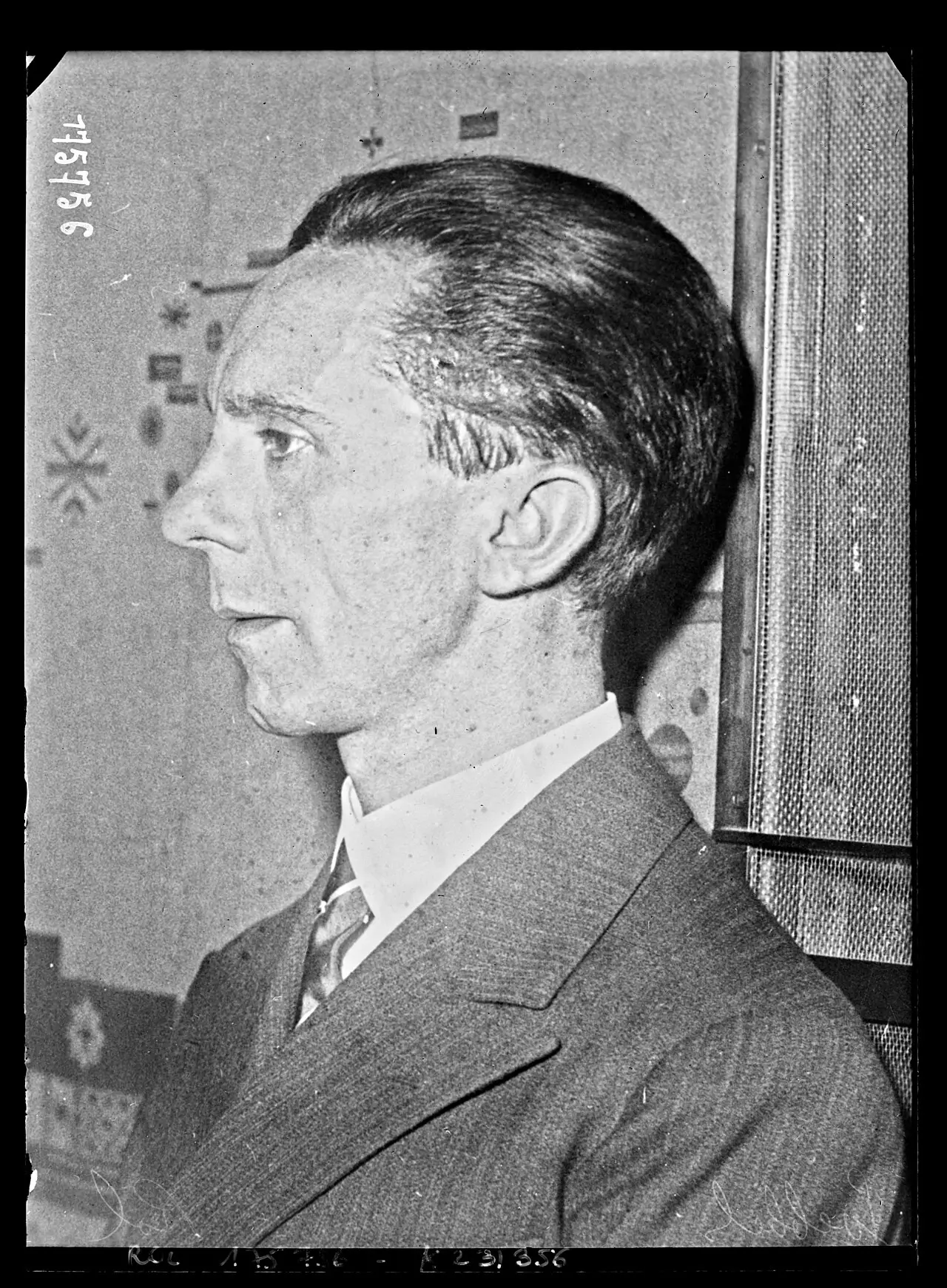 Profile portrait of a thin-faced man with slicked-back dark hair, in a pinstriped suit