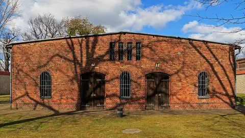 A single-storey red-brick building with two arched wooden doors and arched windows, on a lawn