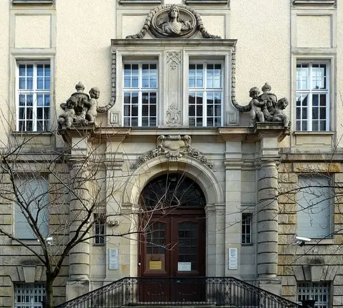 An arched wooden door at the top of a short flight of steps, framed by carved stone with cherub figures above; small plaques hang on either side of the door.