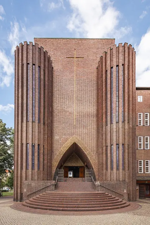 The tall brick front of the church with a steep pointed-arch portal and closely ribbed vertical piers.