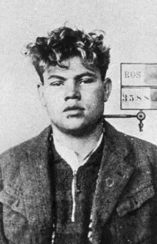 Head-and-shoulders police photograph of a young man with thick curly hair in a rough jacket, with a numbered identification board behind his shoulder.