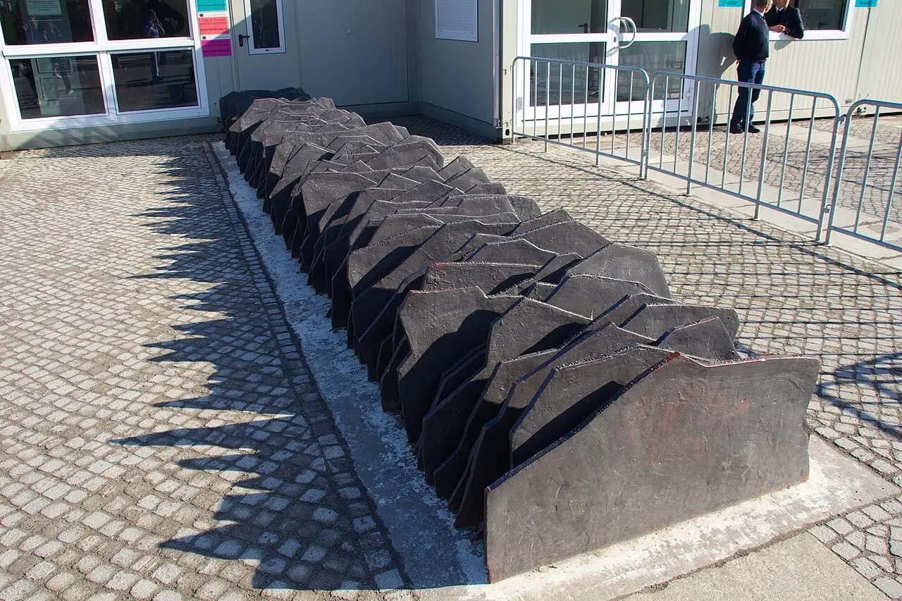 A long row of upright dark metal plates set close together like books on a shelf, in front of a lawn