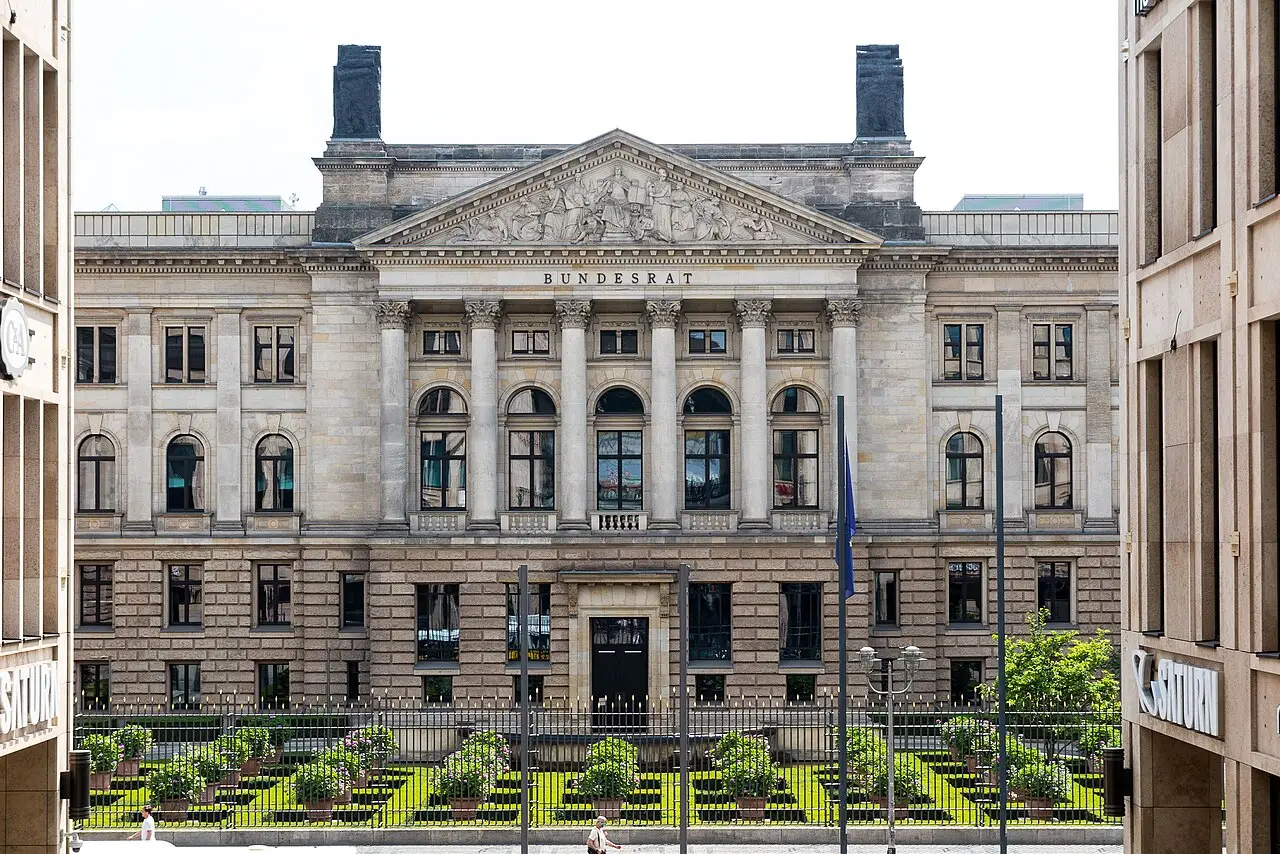 A large neoclassical building with a columned central portico behind a forecourt garden.
