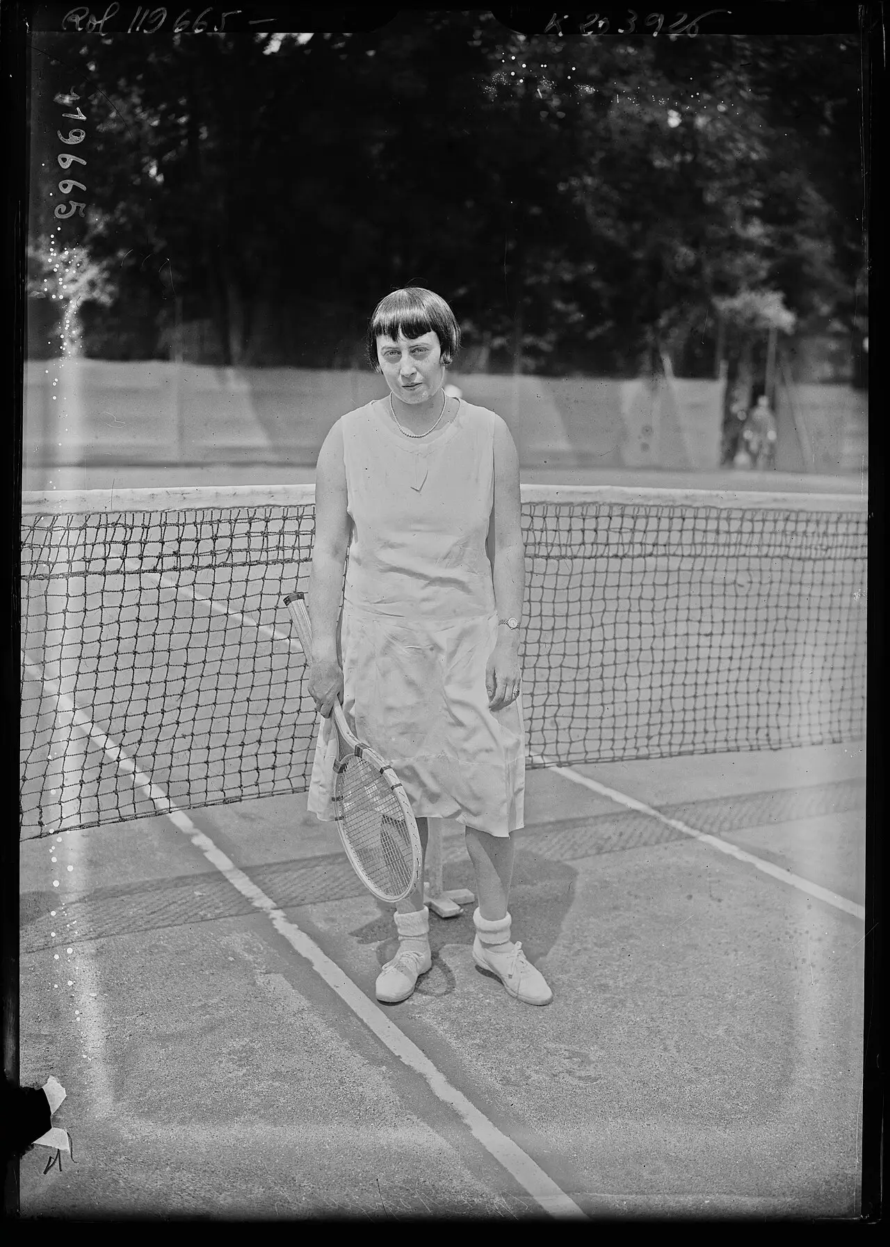 A woman in a white tennis dress and headband on a tennis court