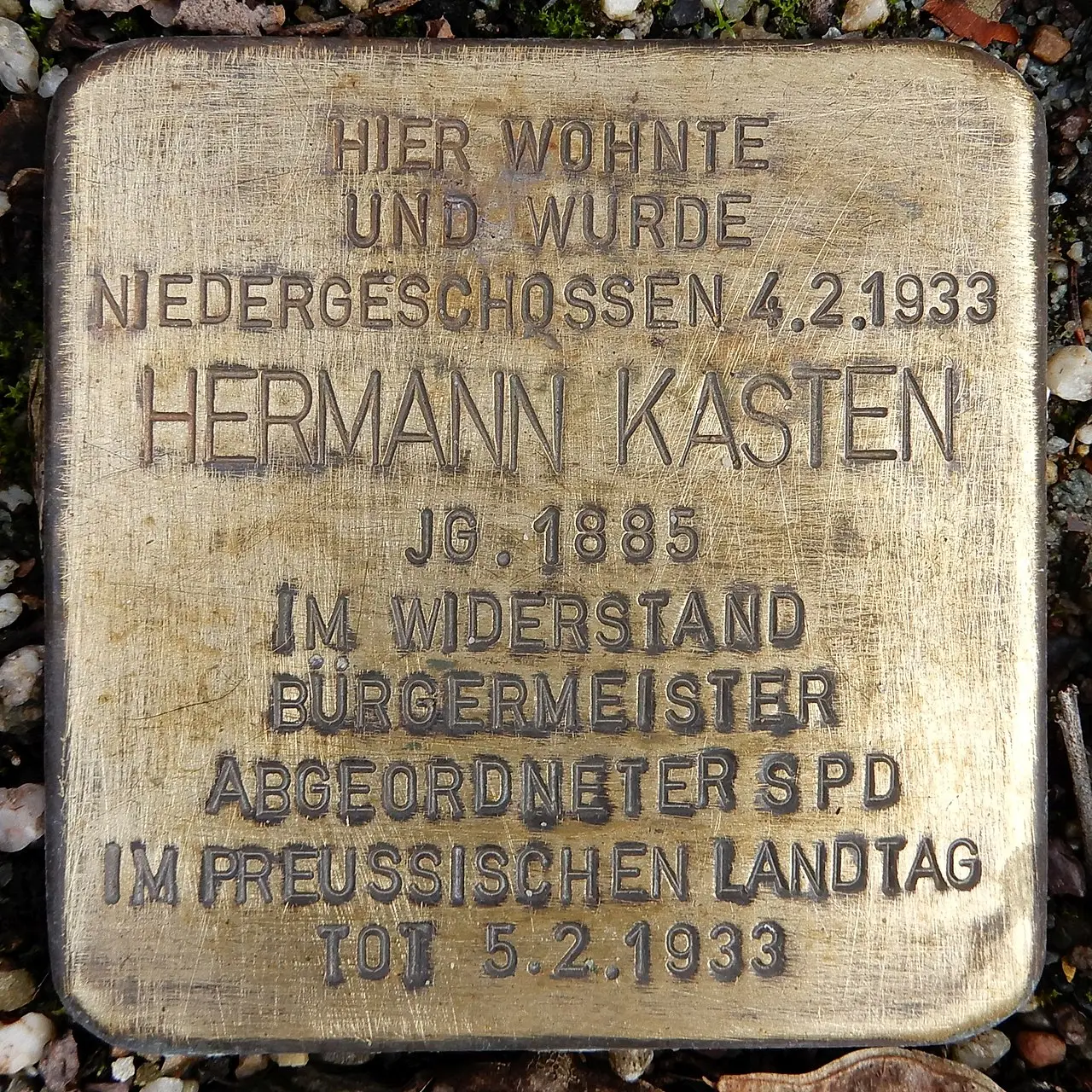 A small brass paving stone engraved with a name and dates, set among cobbles