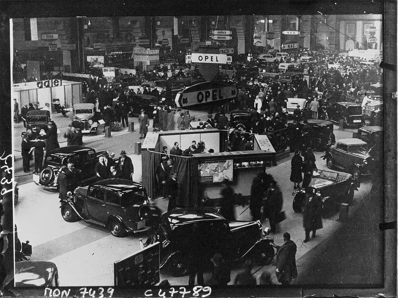 A crowded exhibition hall with rows of cars beneath a high roof